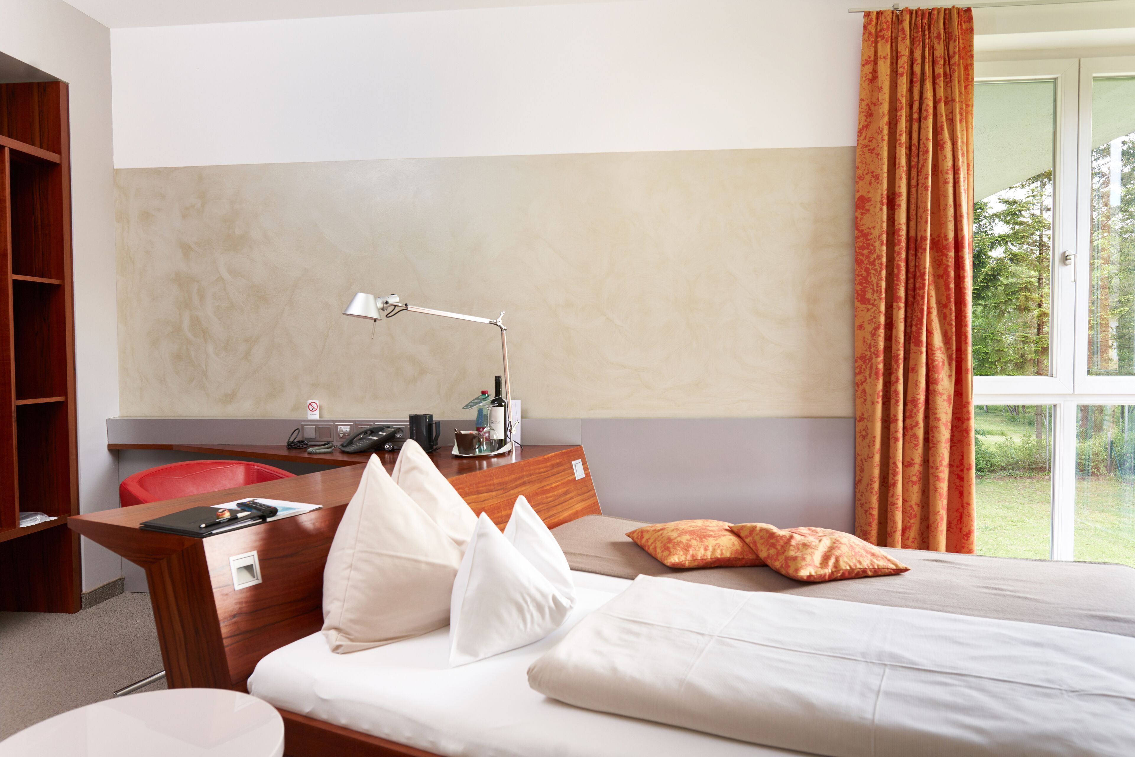 A hotel room with a bed, a desk, a chair, a lamp, and a window with curtains.