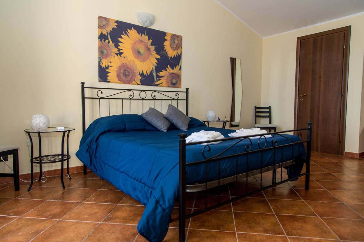 A bedroom with a bed, a wall-mounted painting, a door, and a tiled floor.