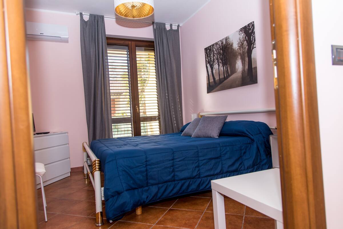 A bedroom with a bed, a desk, a chair, a dresser, and a window with curtains.