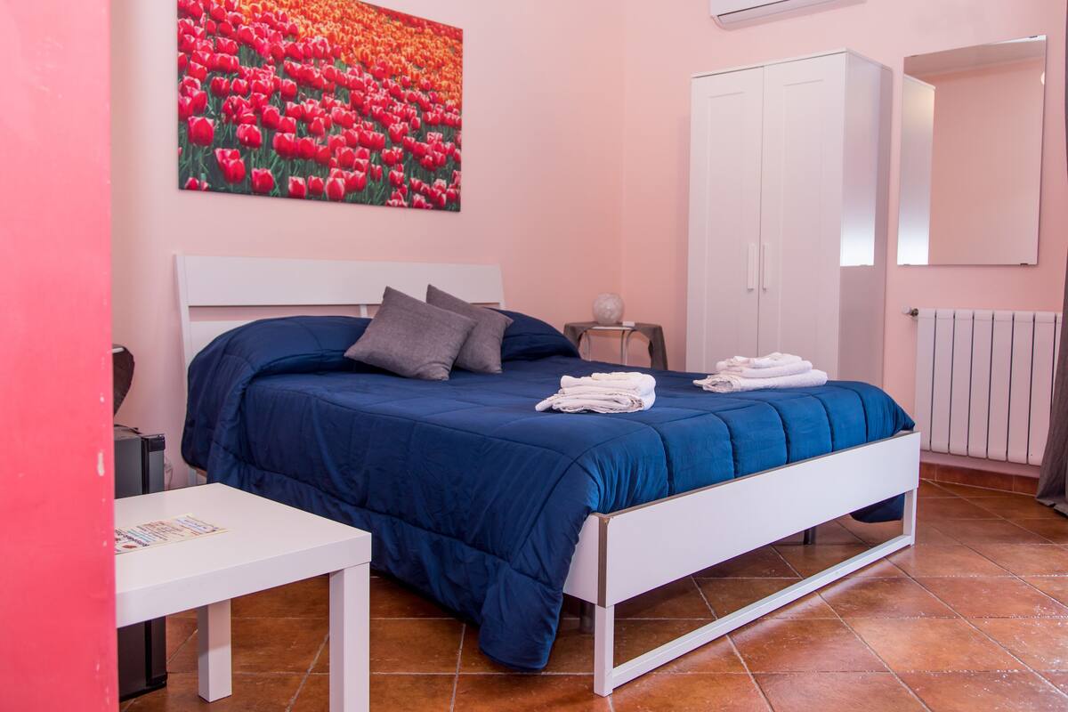 A bedroom with a bed, a nightstand, a white wardrobe, and a painting of tulips on the wall.