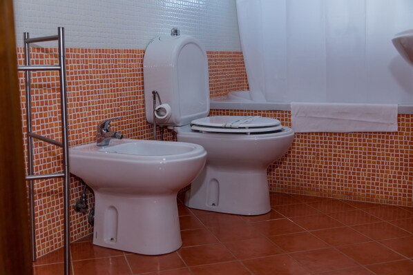 Un baño con dos inodoros, un bidé, un perchero para toallas y una cortina de ducha.