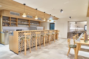 A modern bar area with a long counter, multiple bar stools, and shelves stocked with bottles and glasses.