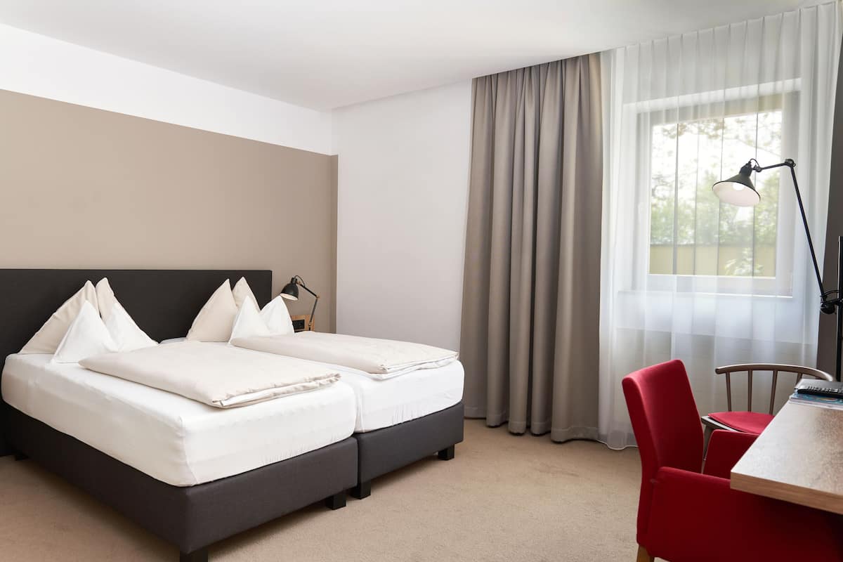 A hotel room with a bed, a desk, a chair, and a window with curtains.