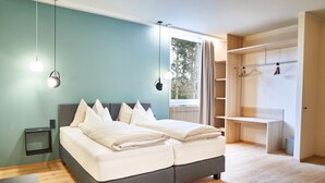 A modern bedroom with a grey bed, white bedding, a small bedside table, and a wardrobe with a light wood finish. - Gasthof Maxlhaid (Wels)