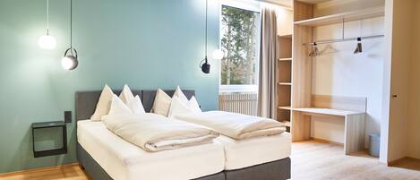 Un dormitorio moderno con una cama gris, ropa de cama blanca, una mesita de noche pequeña y un armario con acabado en madera clara.