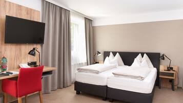 Habitación de hotel con cama, escritorio, silla, televisor y ventana con cortinas.