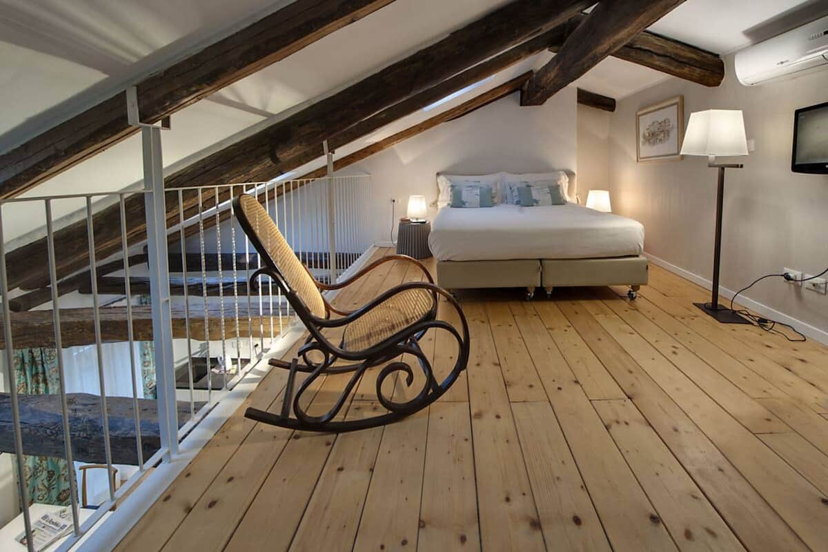 Une chambre avec un plancher en bois, un lit, un fauteuil à bascule, une table de chevet, une lampe et un téléviseur.
