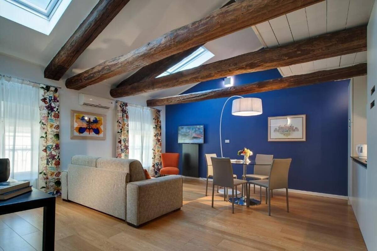 Un salon avec un mur bleu, des poutres en bois, un canapé, une table à manger avec des chaises et un téléviseur.