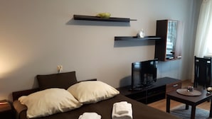 A hotel room with a bed, a TV, a small table, and a shelf with a fruit bowl. - Jm Apartamenty (Szczecin)