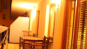 A balcony with a wooden table and chairs, a bench, and a sliding glass door with blinds. - Jm Apartamenty (Szczecin)