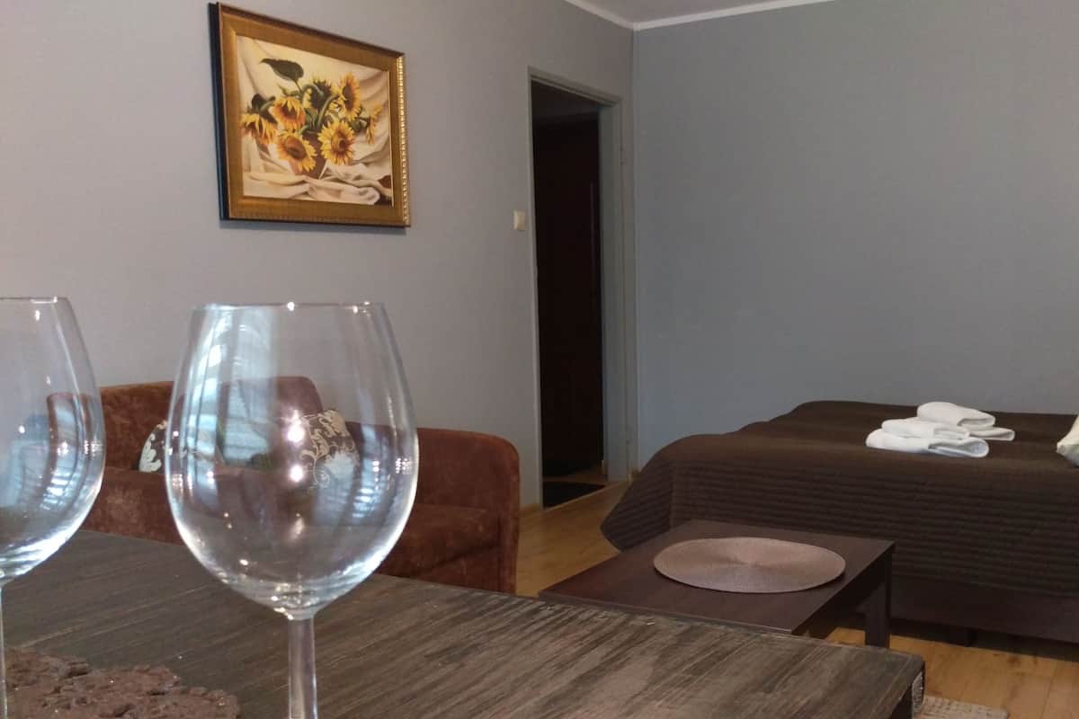 A hotel room with a bed, a table with two wine glasses, a painting on the wall, and a door leading to another room.