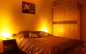 A bedroom with a bed, two bedside lamps, a wooden wardrobe, and a wall-mounted artwork.