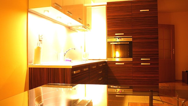 A modern kitchen with wooden cabinets, stainless steel appliances, and a glass countertop. - Jm Apartamenty (Szczecin)