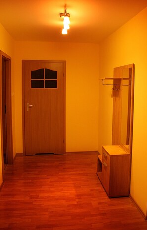 A hallway with wooden flooring, a wooden door with a window, and a mirror on the wall.
