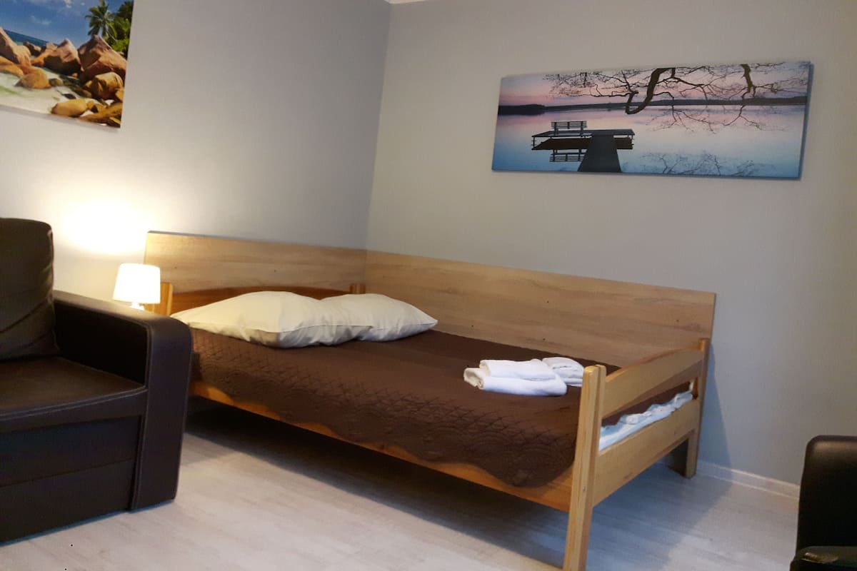 A single bed with a wooden headboard, a nightstand with a lamp, and two paintings on the wall.
