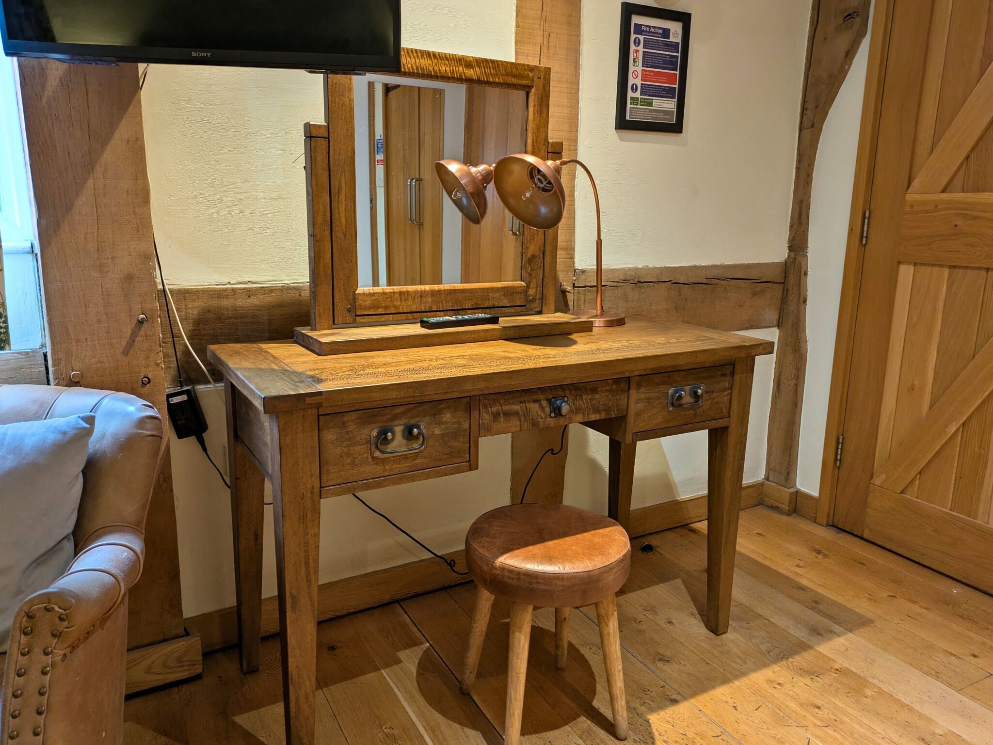 A wooden desk with a mirror, a lamp, and a remote control.