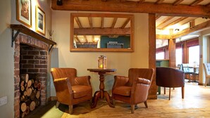 Une pièce chaleureuse avec une cheminée en briques, deux fauteuils en cuir, une table en bois et un grand miroir au mur.