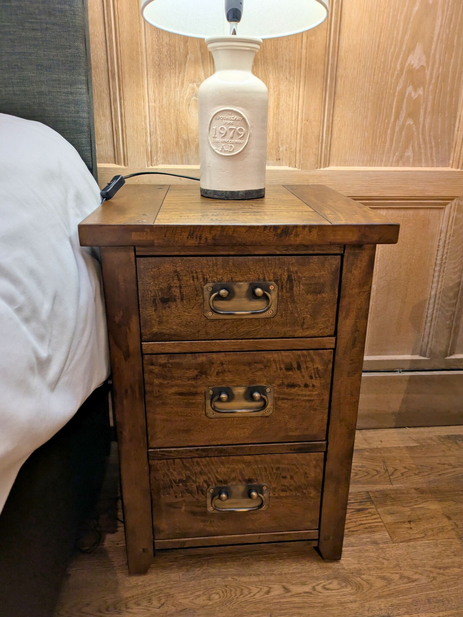 A wooden nightstand with a lamp and a bed.