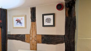 Une pièce avec des poutres apparentes, un radiateur, un canapé en cuir marron et deux tableaux encadrés au mur.