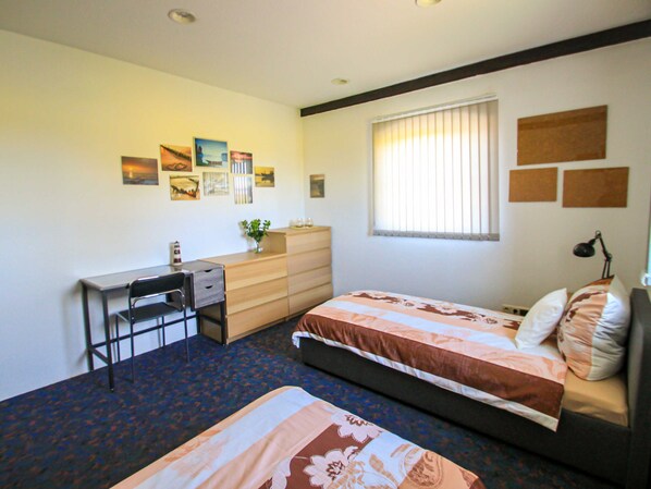 A bedroom with a bed, a desk, and a chair. There are pictures on the wall and a window with blinds.