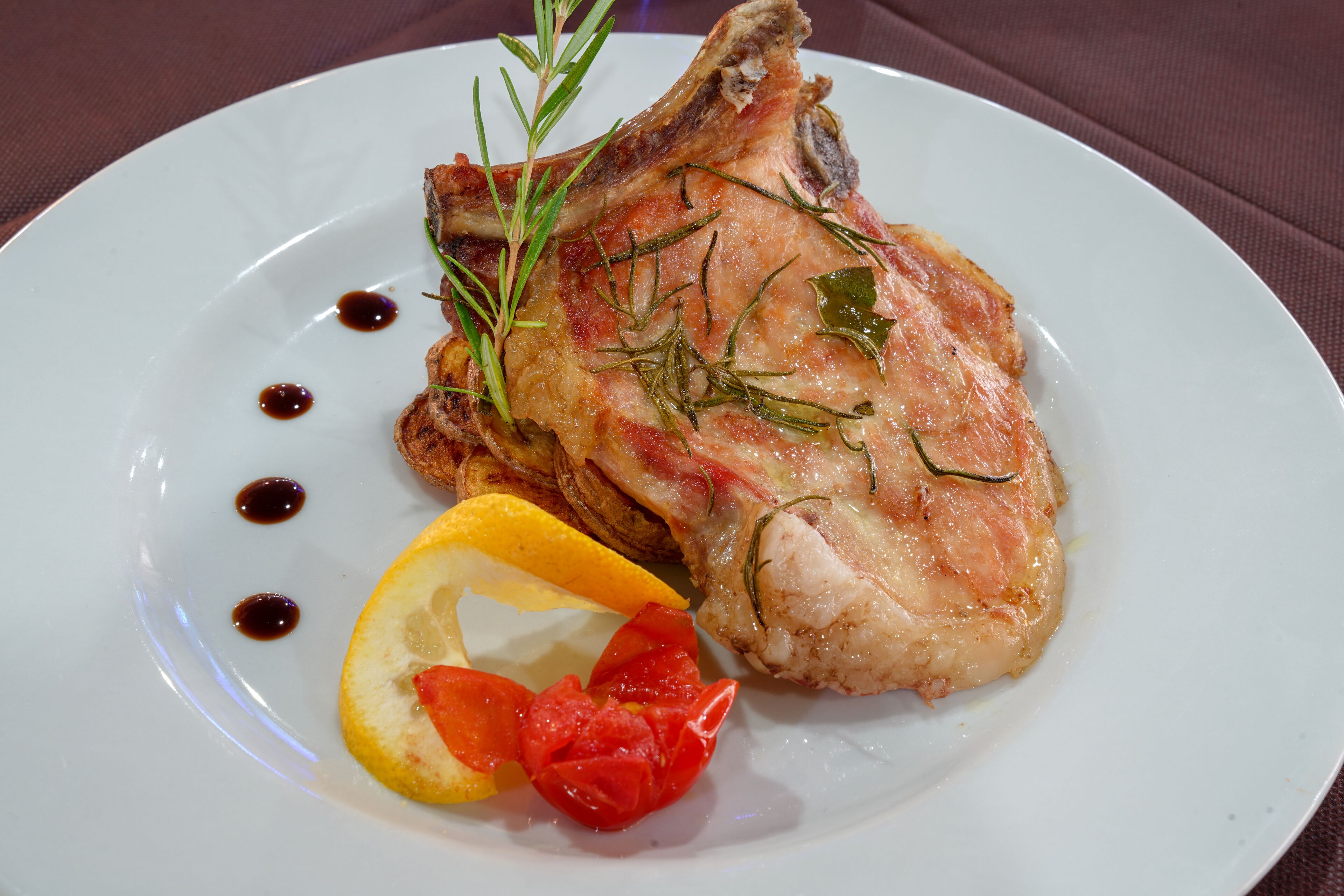 A plate with a cooked meat dish, garnished with herbs and accompanied by lemon and tomato slices.