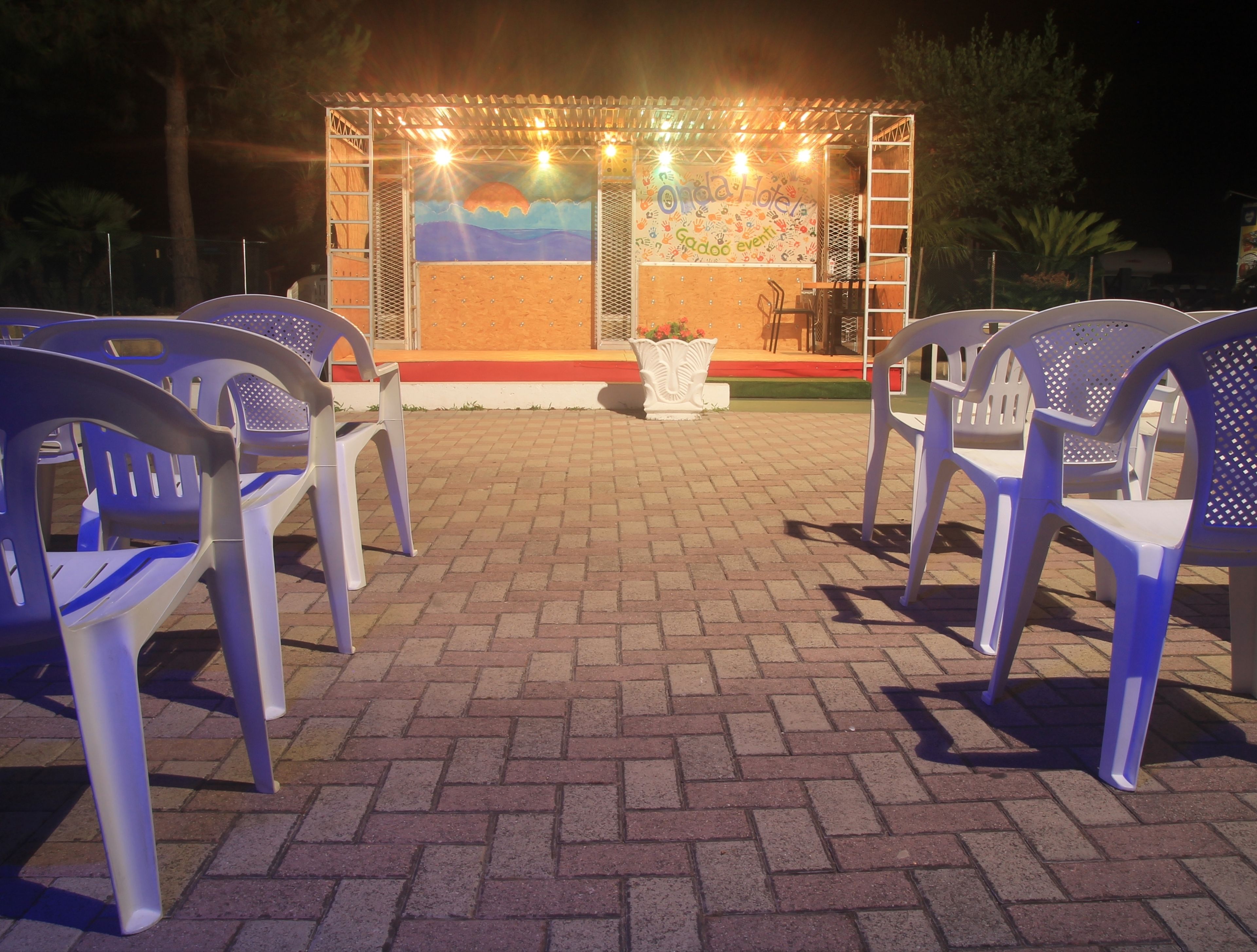 A stage with a mural, surrounded by plastic chairs and a brick floor.
