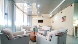A modern living room with two grey sofas, a wooden coffee table, and a flat-screen TV mounted on the wall. - Onda Hotel (Silvi)