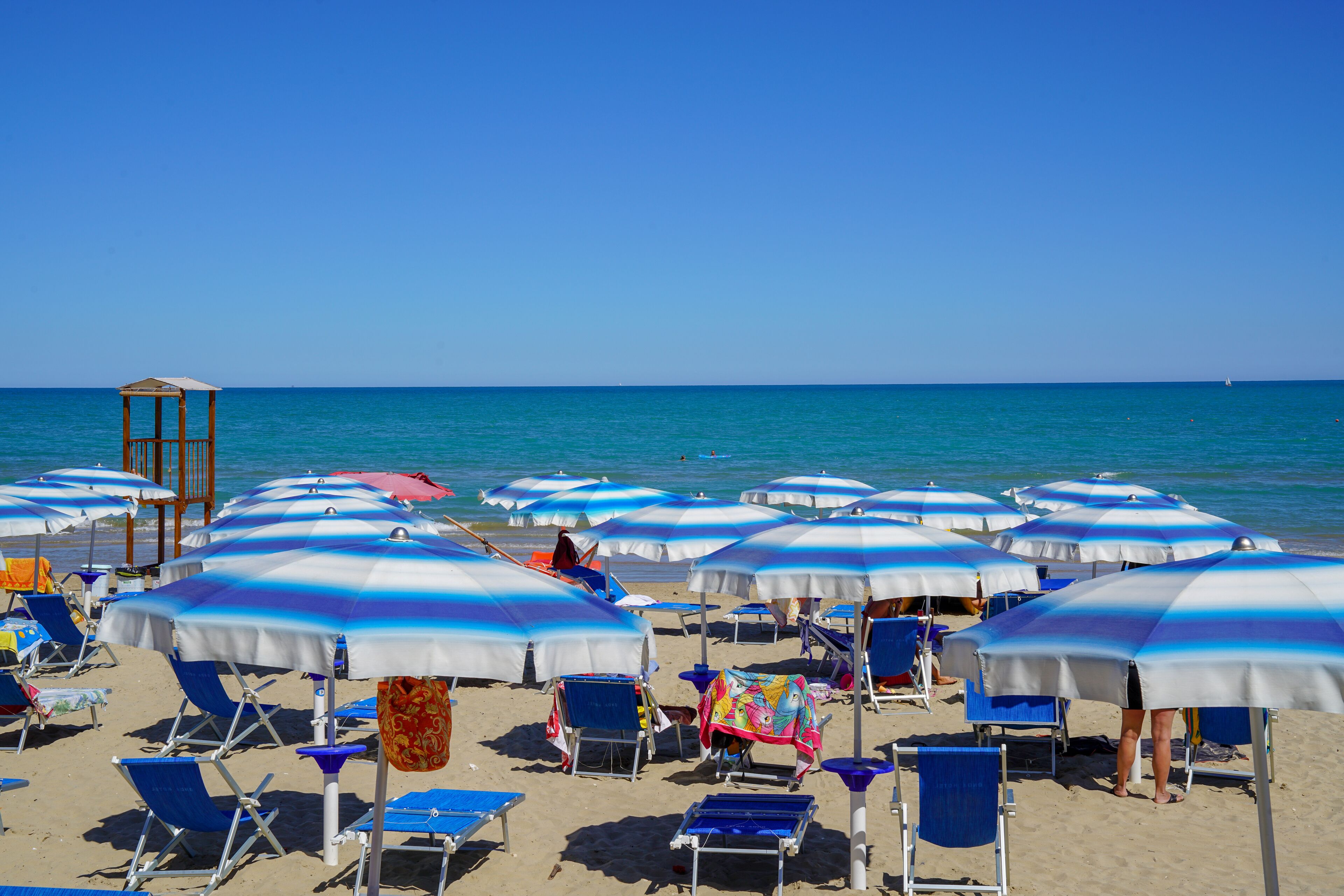 Une plage avec de nombreux parasols bleus et blancs à rayures, des chaises de plage et une structure en bois.