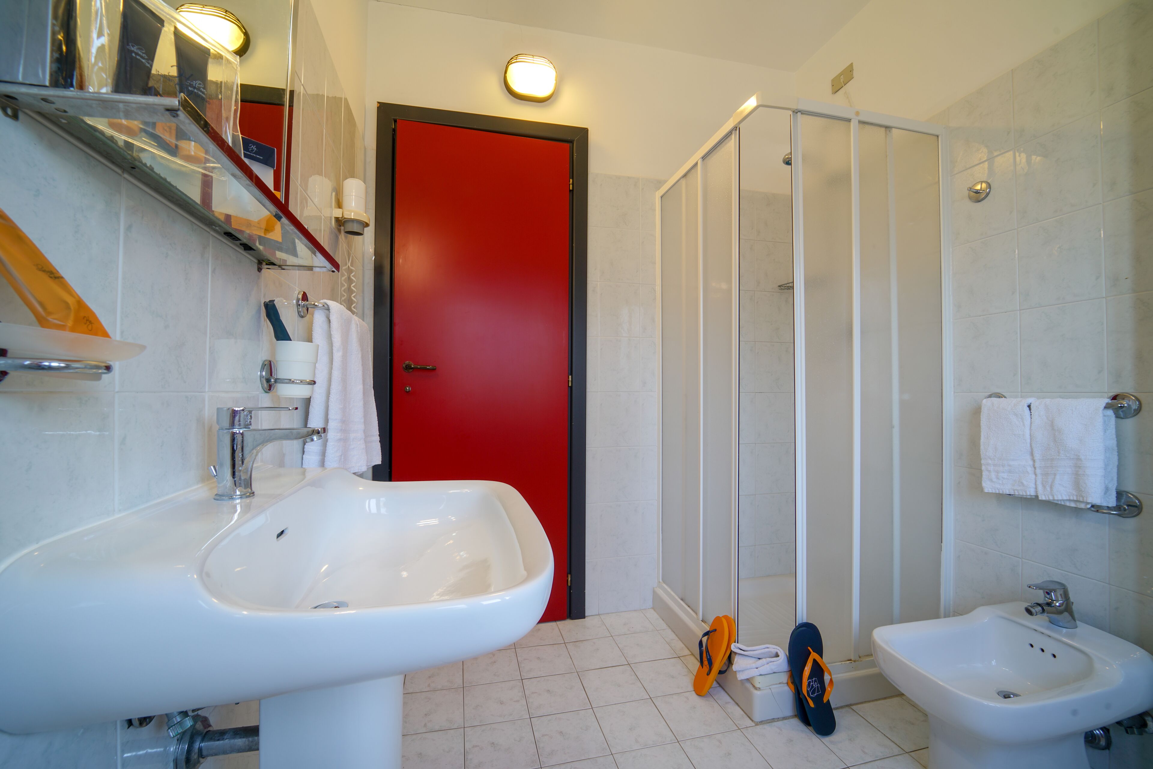 A bathroom with a red door, two sinks, a shower, and a towel rack.