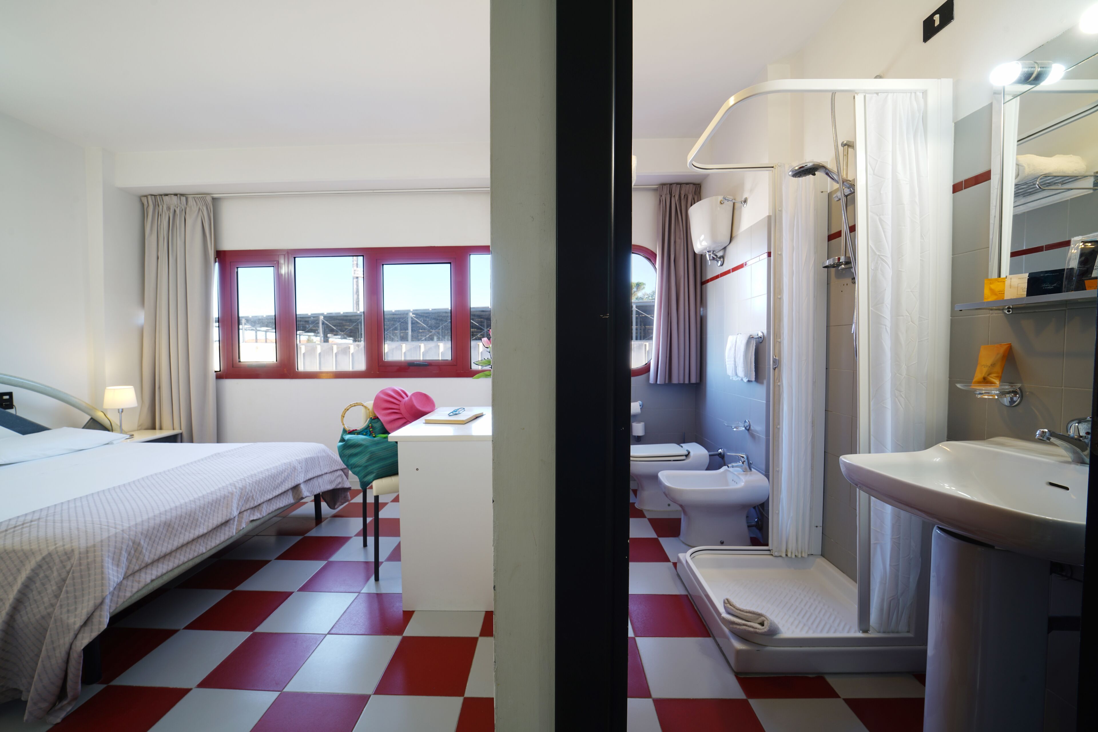 Habitación de hotel con cama, escritorio, silla y baño completo con lavamanos, inodoro y ducha.