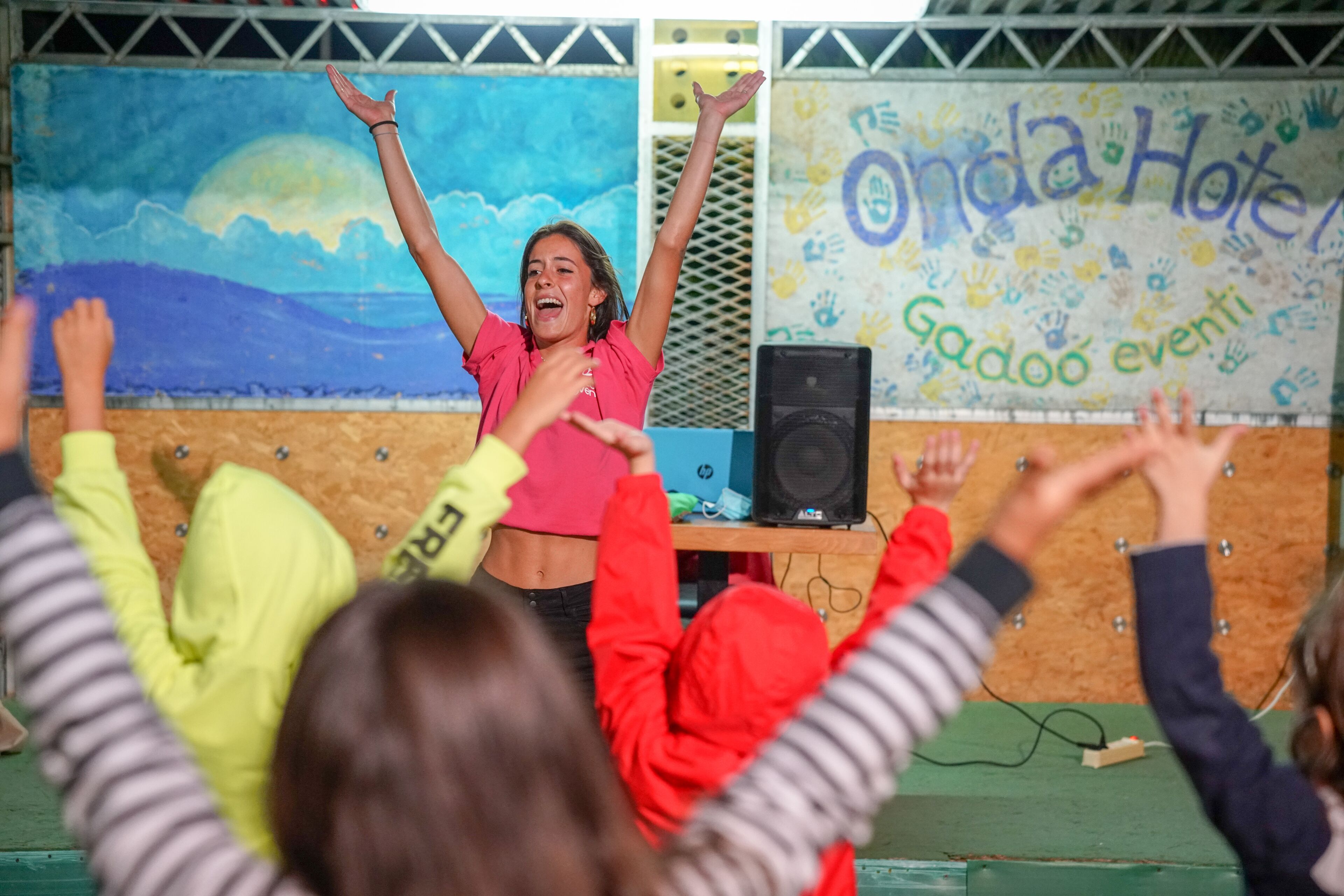 Un escenario con una persona con camisa rosa y un fondo que muestra 'Onda Hotel' y 'Gadoo events' escritos.