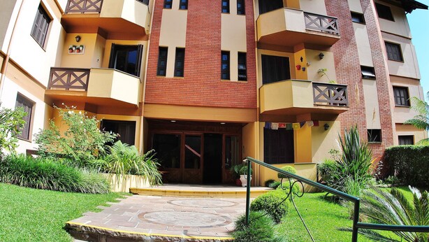 A multi-story building with balconies, a central entrance, and surrounding greenery. - Apartamento Serra - Gramado (Gramado)