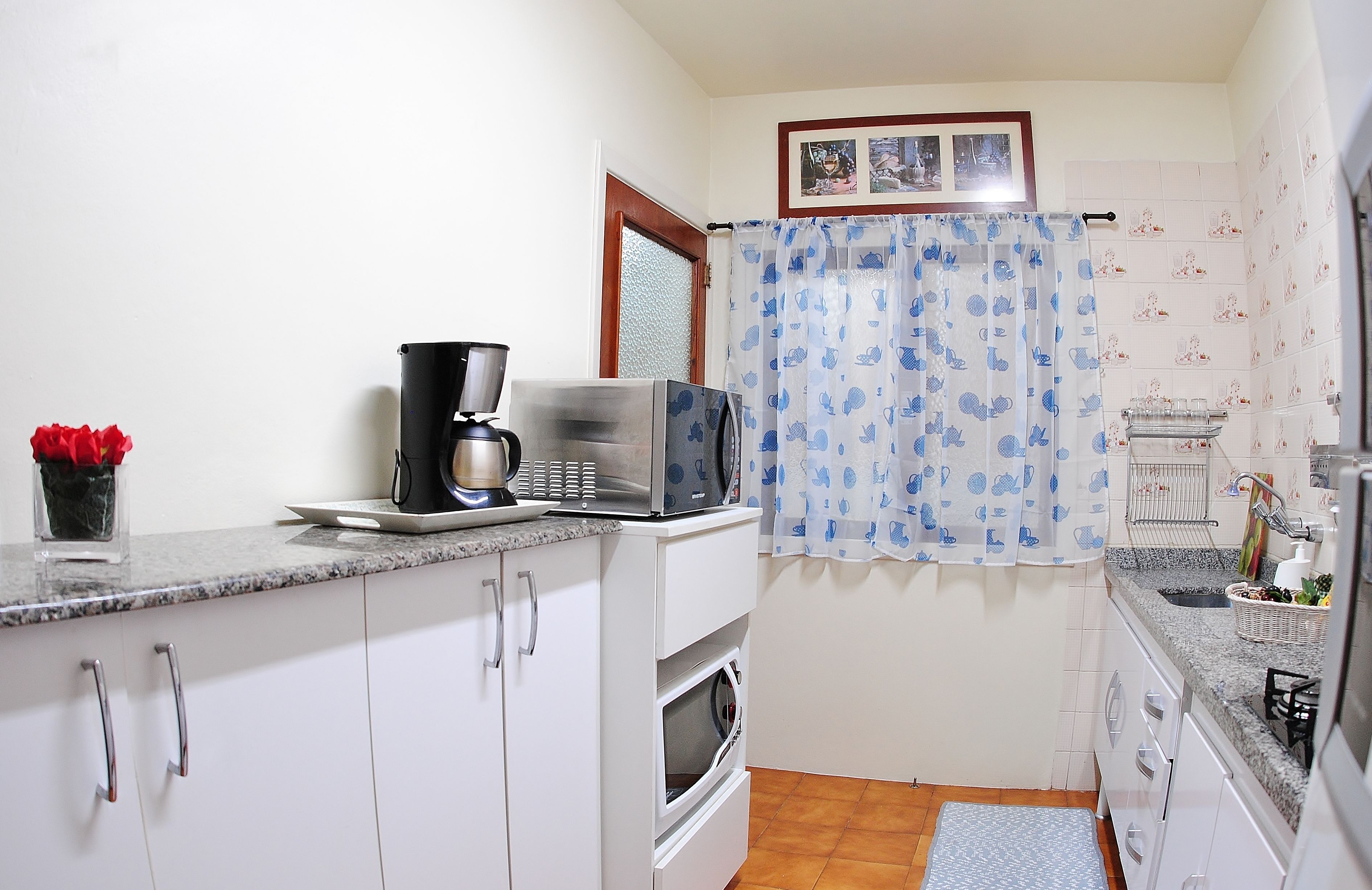 Una cocina compacta con armarios blancos, un microondas, una cafetera y un horno pequeño.