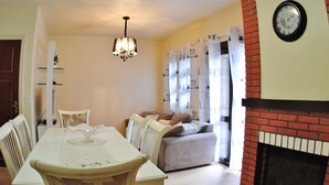 A dining area with a table, chairs, a chandelier, a sofa, and a fireplace. - Apartamento Serra - Gramado (Gramado)