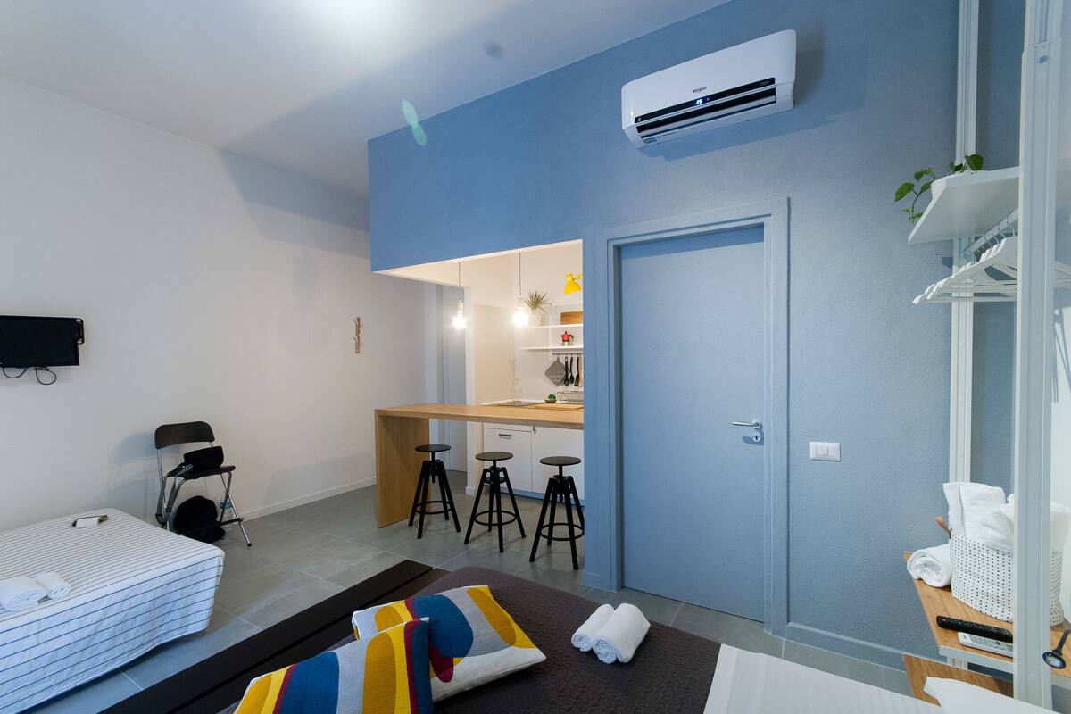 A modern hotel room with a bed, a desk, and a kitchenette.