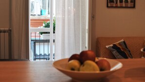 A living room with a view of a balcony, a bowl of fruit on the table, and a framed plant on the wall. - Capofortuna B&B (Salerno)