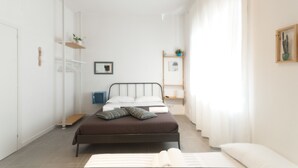 A minimalist bedroom with a bed, a bedside table, a wardrobe, and a shelf with plants. - Capofortuna B&B (Salerno)