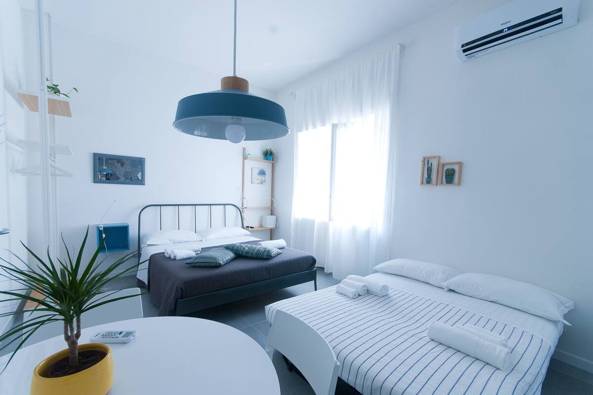 A modern hotel room with a bed, bedside table, and a potted plant.