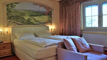 A bedroom with a large bed, a chair, a nightstand, and a painting of a landscape on the wall.