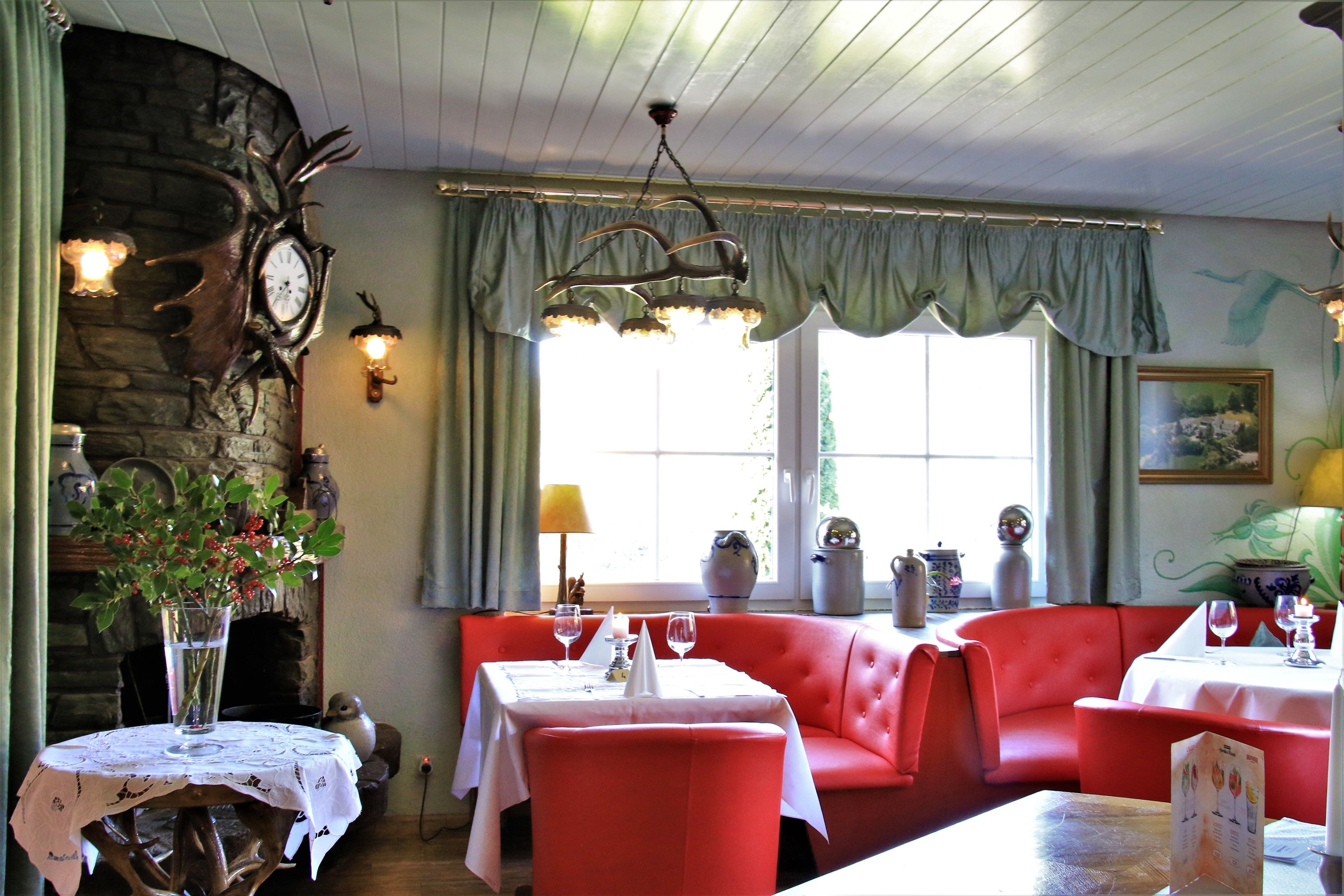 Un espace repas avec un coin salon rouge, une table ronde recouverte d’une nappe blanche et un lustre.