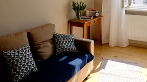 Un salon avec un canapé, une petite table sur laquelle est posée une plante, et deux œuvres d’art encadrées accrochées au mur.