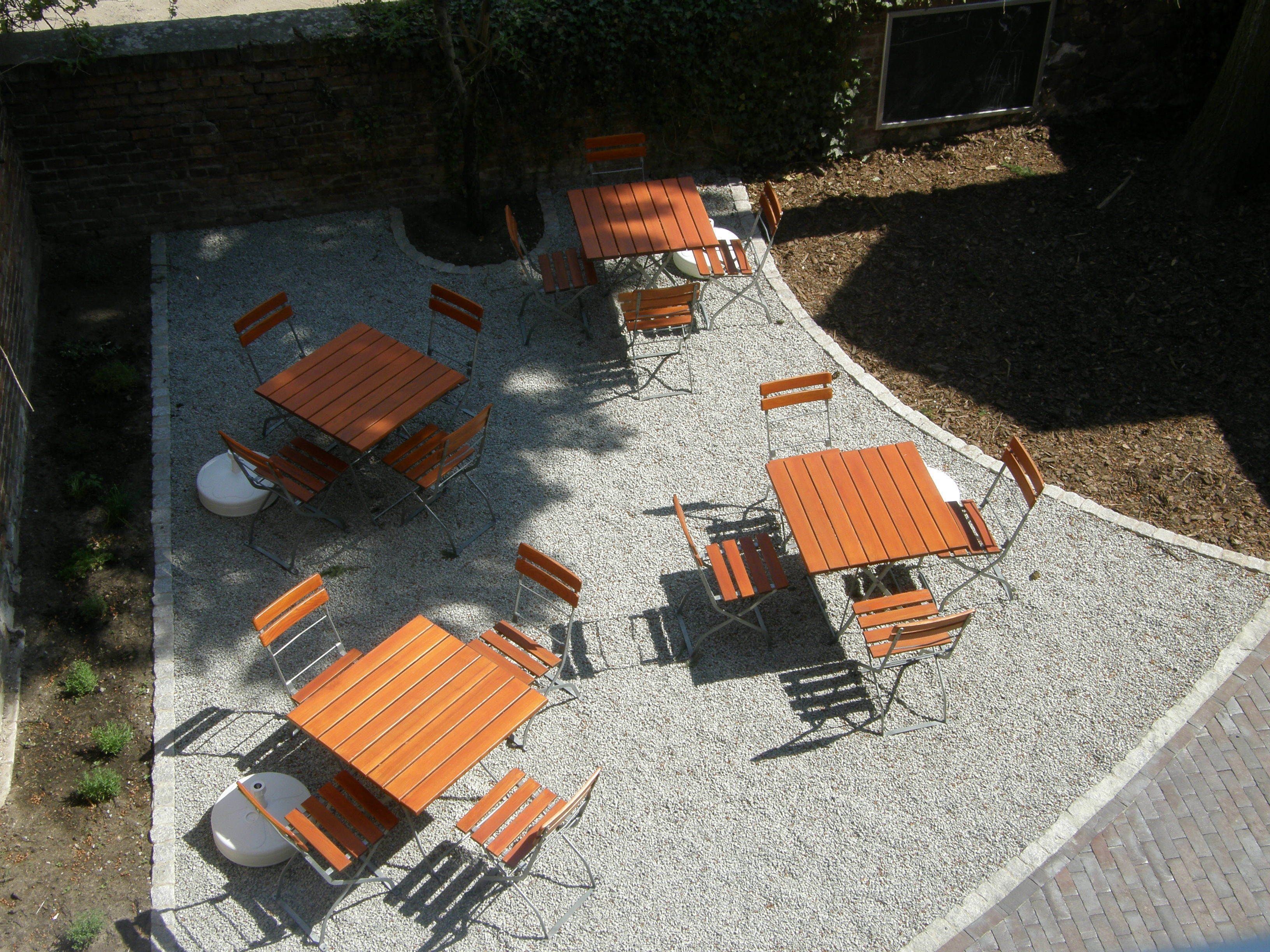 Un patio al aire libre con varias mesas y sillas de madera dispuestas sobre un suelo de grava.