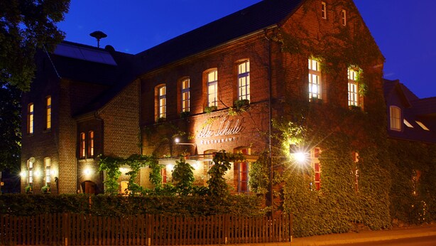 Tiilirakennus, jonka yläpuolella on kyltti, jossa lukee: ”Mitte Schule Restaurant”. Siinä on useita ikkunoita, ja se on ympäröity puuaitalla.