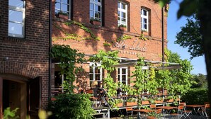 Tiilestä rakennettu rakennus, jossa on ulkona istumapaikkoja ja kyltti, jossa lukee: ”Alte Schule”.