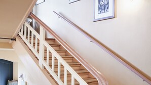 Portaat, joissa on puiset askelmat ja valkoiset kaiteet, johtavat ylätasanteelle, jonka seinällä on kehystettyjä valokuvia.
