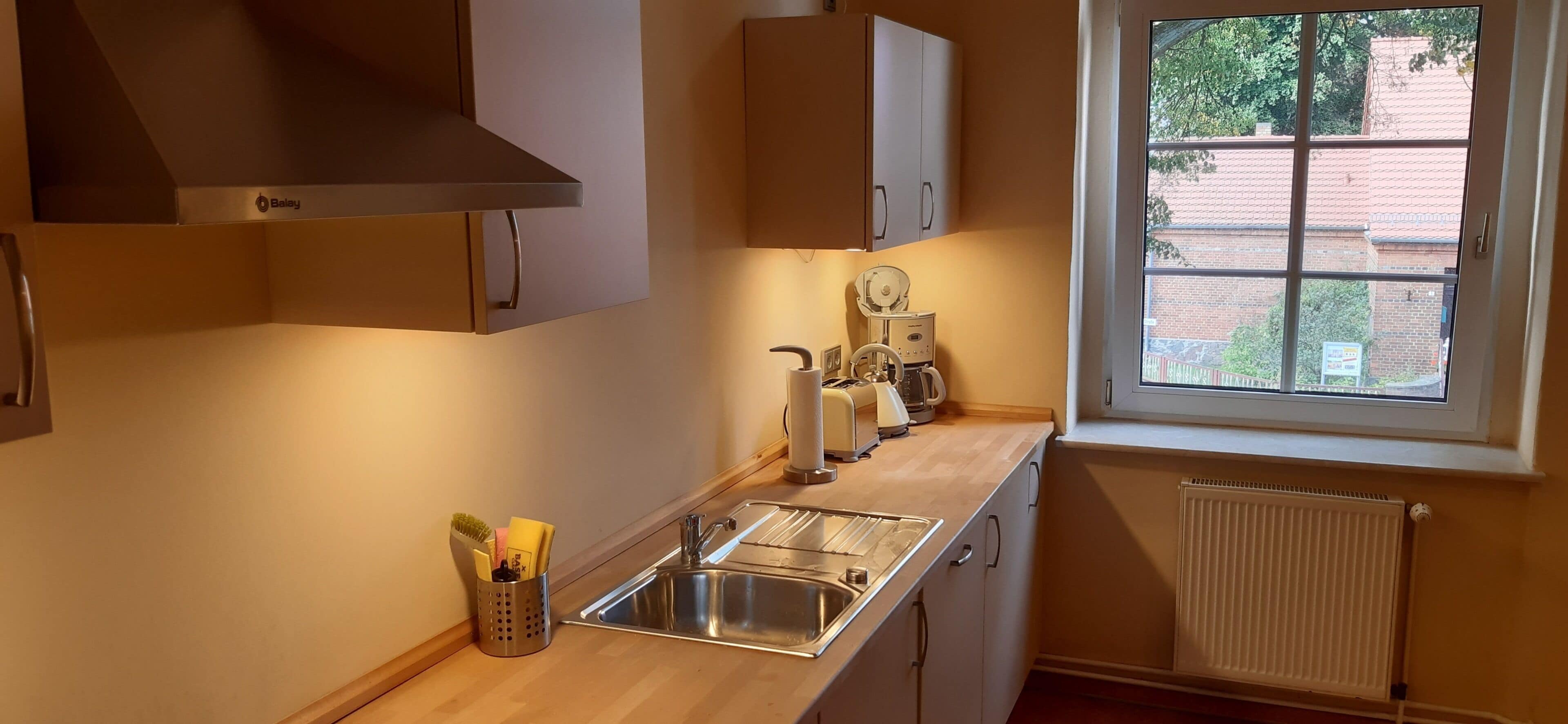 Una cocina con un lavamanos, armarios, una ventana y un radiador.