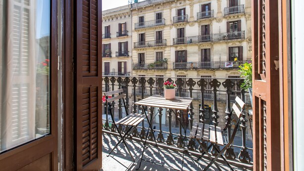 A balcony with a table and chairs, a potted plant, and a view of a building with multiple balconies.