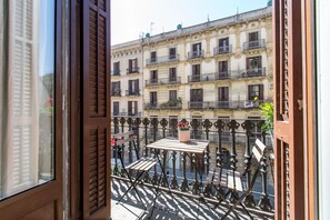 Ein Balkon mit Tisch und Stühlen, einer Topfpflanze und Blick auf ein Gebäude mit mehreren Balkonen.