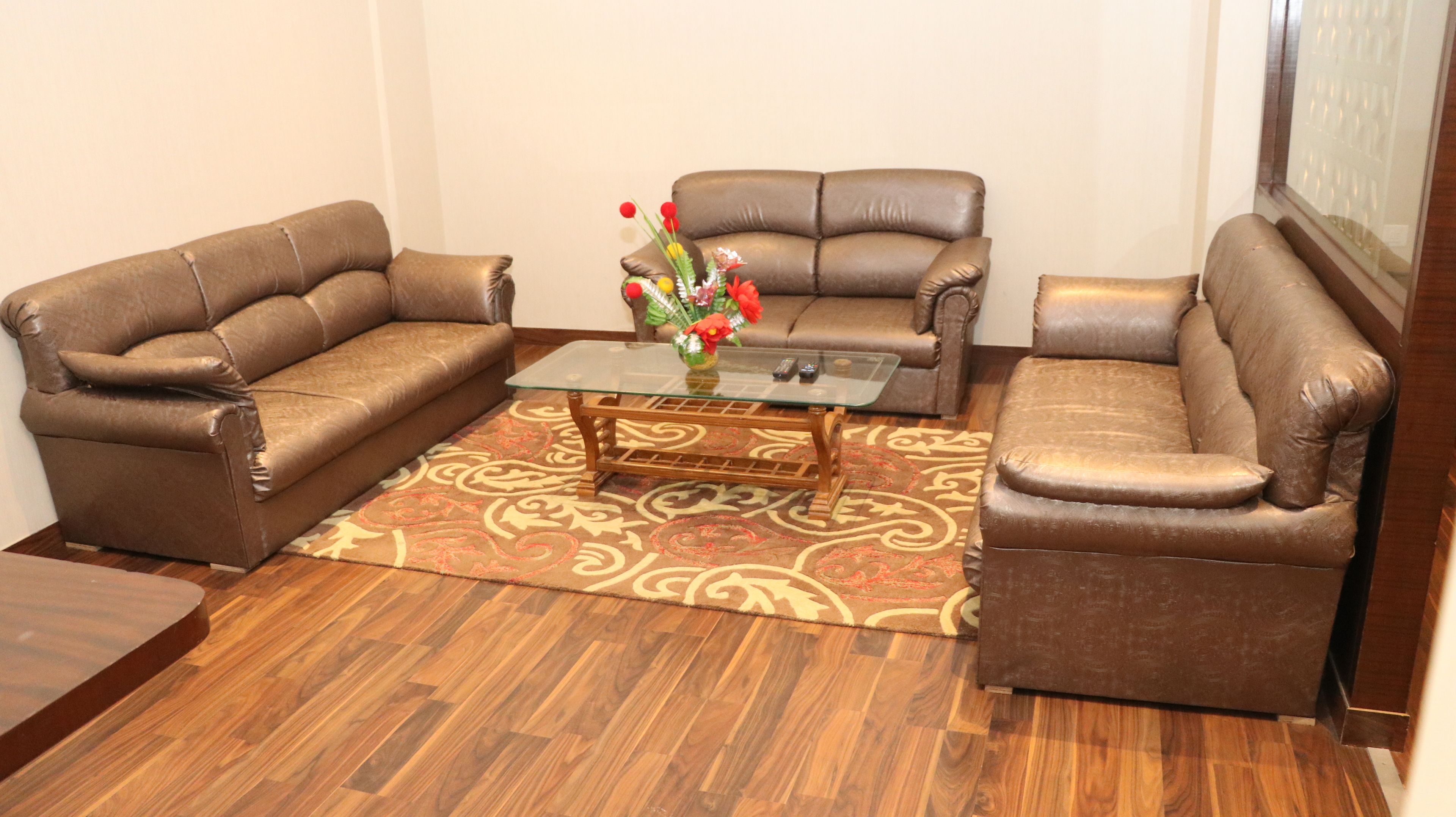 A living room with two brown leather sofas, a glass coffee table, and a patterned rug.