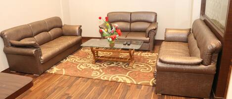 A living room with two brown leather sofas, a glass coffee table, and a patterned rug.